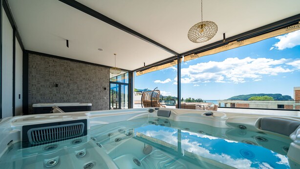 Una piscina interior moderna con paredes de vidrio transparente, pared de piedra y vista al cielo y montañas.