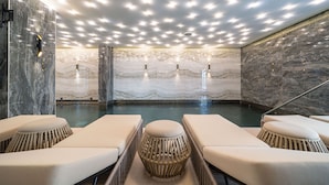 Un área de spa con paredes de mármol, piscina y sillones de descanso.