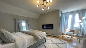 Een slaapkamer met een bed, een aan de muur bevestigde televisie en een raam met gordijnen.