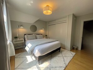 A modern bedroom with a bed, bedside tables, a mirror, and a ceiling light.