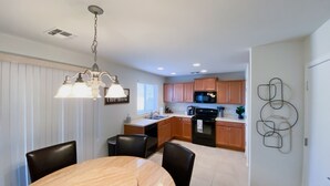 Une cuisine moderne avec des meubles en bois, une cuisinière noire et un coin repas comprenant une table ronde et des chaises.