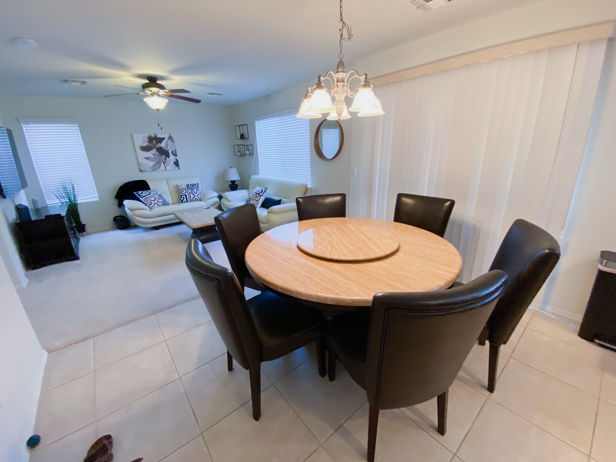 A dining area with a round wooden table and six chairs, a ceiling fan, and a chandelier.