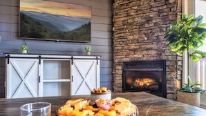A rustic interior with a stone fireplace, a dining table with a fruit platter, and a mounted painting.