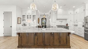 A modern kitchen with white cabinetry, a large island with a marble countertop, and two pendant lights. - The Shoreland Water-Front Home, Volleyball &Hottub (Gulf Shores)