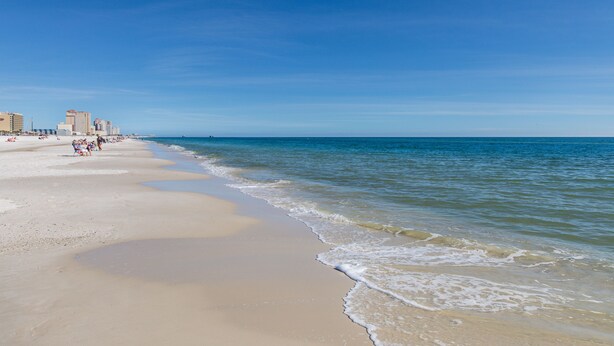 A beach with a clear sky, sandy shore, and buildings in the background. - The Shoreland Water-Front Home, Volleyball &Hottub (Gulf Shores)