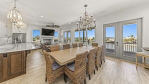 A spacious kitchen with a large island, modern appliances, and a dining area with wicker chairs and a wooden table. - The Shoreland Water-Front Home, Volleyball &Hottub (Gulf Shores)