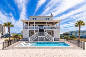 A two-story beachfront property with a swimming pool, a staircase leading to the upper level, and a sandy beach area.