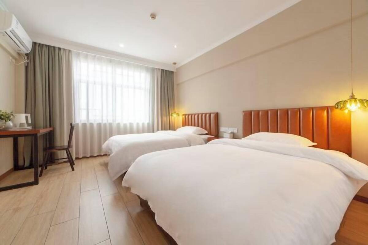 A hotel room with two beds, a desk, a chair, and a window with curtains.