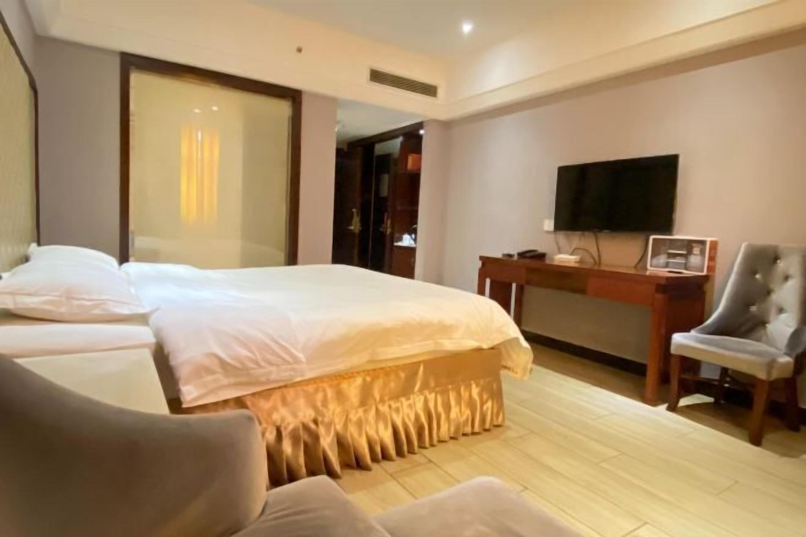 Habitación de hotel con una cama grande, un escritorio con silla, un televisor y un armario.
