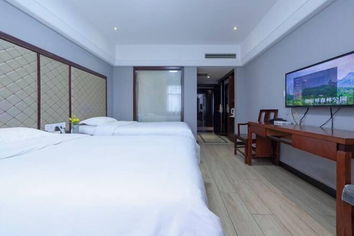 A hotel room with two beds, a desk, a television, and a view of a mountain landscape.