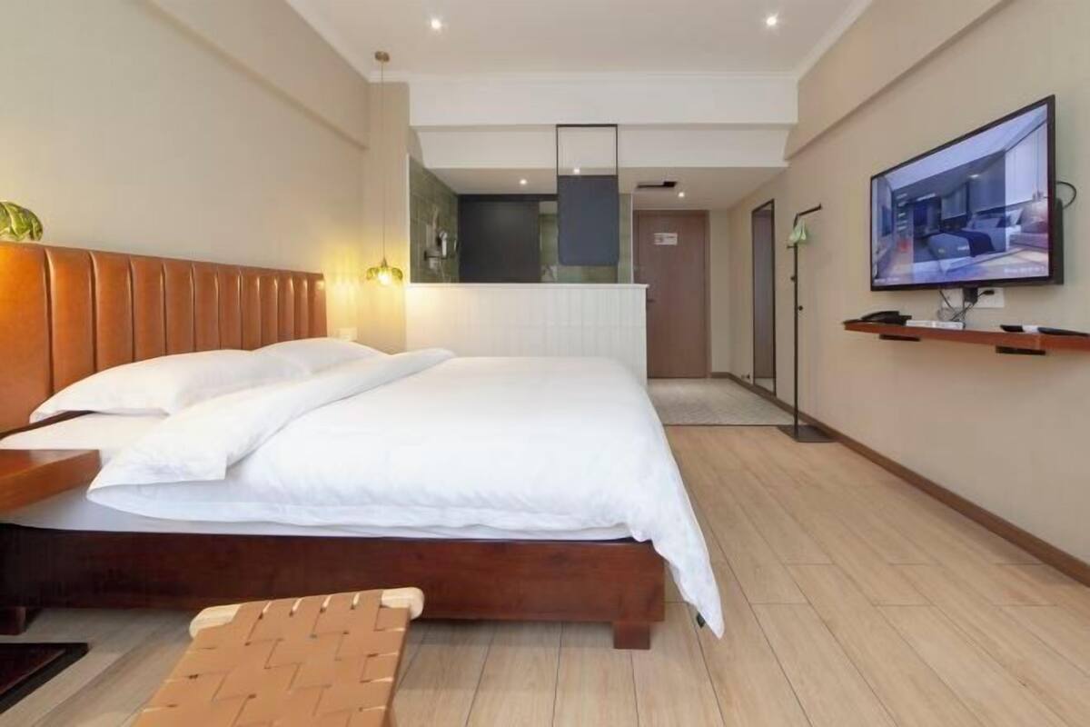 A modern hotel room with a wooden bed, a flat-screen TV, a small kitchenette, and a large mirror.
