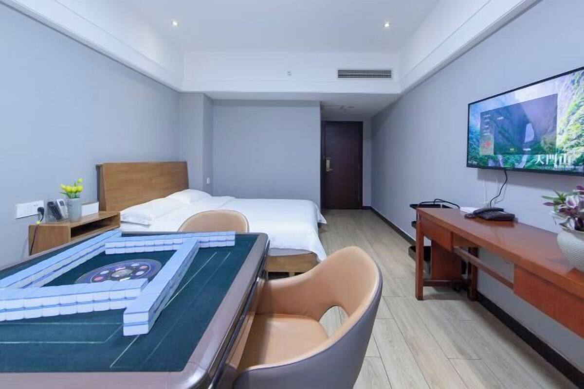 A hotel room with a bed, a desk with a computer, a television, and a table with a board game.
