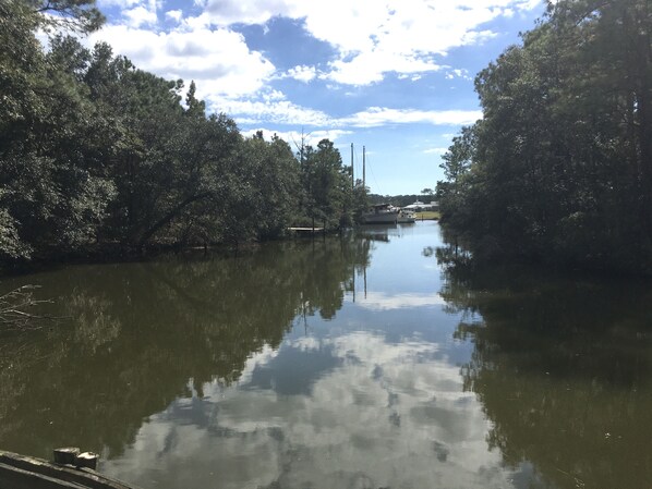 Un río tranquilo con árboles densos a ambos lados, una pequeña embarcación amarrada a la derecha, y un cielo despejado.