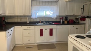 Una cocina con armarios blancos, una ventana con cortina, un fregadero y una estufa.