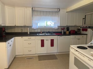 A kitchen with white cabinets, a window with a curtain, a sink, and a stove.