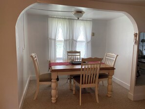 A dining area with a table and four chairs, a ceiling fan, and a window with sheer curtains.