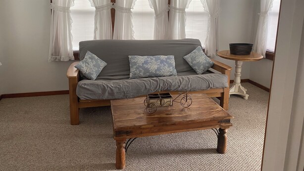 Una habitación con un sofá gris, dos cojines estampados, una mesa de centro de madera y una mesita redonda con un cuenco.