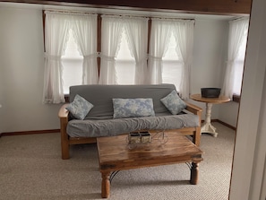 A room with a grey sofa, two patterned cushions, a wooden coffee table, and a small round table with a bowl.