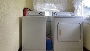 A laundry area with two washing machines, a window with white curtains, and a blue detergent bottle. - Perfect Family Vacation House - Walk to Beach (Sylvan Beach)