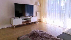 Ein modernes Wohnzimmer mit einem Flachbildfernseher auf einer weißen Konsole, einem flauschigen Teppich und einer Stehlampe.