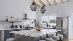 A modern kitchen with a large island, bar stools, a built-in oven, and a refrigerator.
