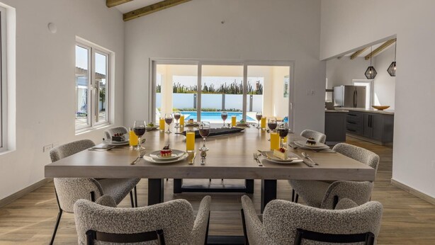 A dining area with a large table, six chairs, and a view of a swimming pool.