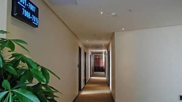 A hotel hallway with a digital sign displaying room numbers, a potted plant, and a carpeted floor.