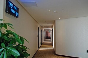 A hotel hallway with a digital sign displaying room numbers, a potted plant, and a carpeted floor. - Ganlu Hotel (Yunan) (Yunan)