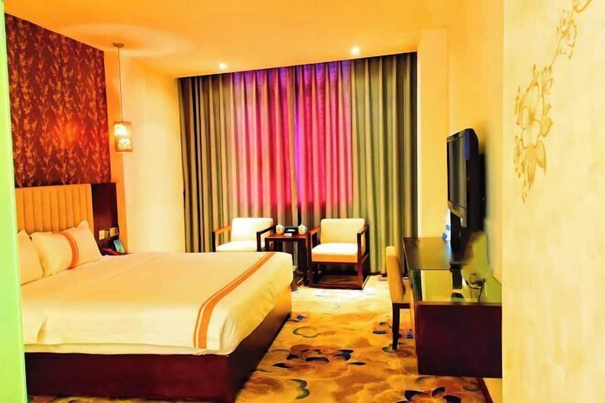 A hotel room with a large bed, two chairs, a small table, a TV, and a curtain backdrop.