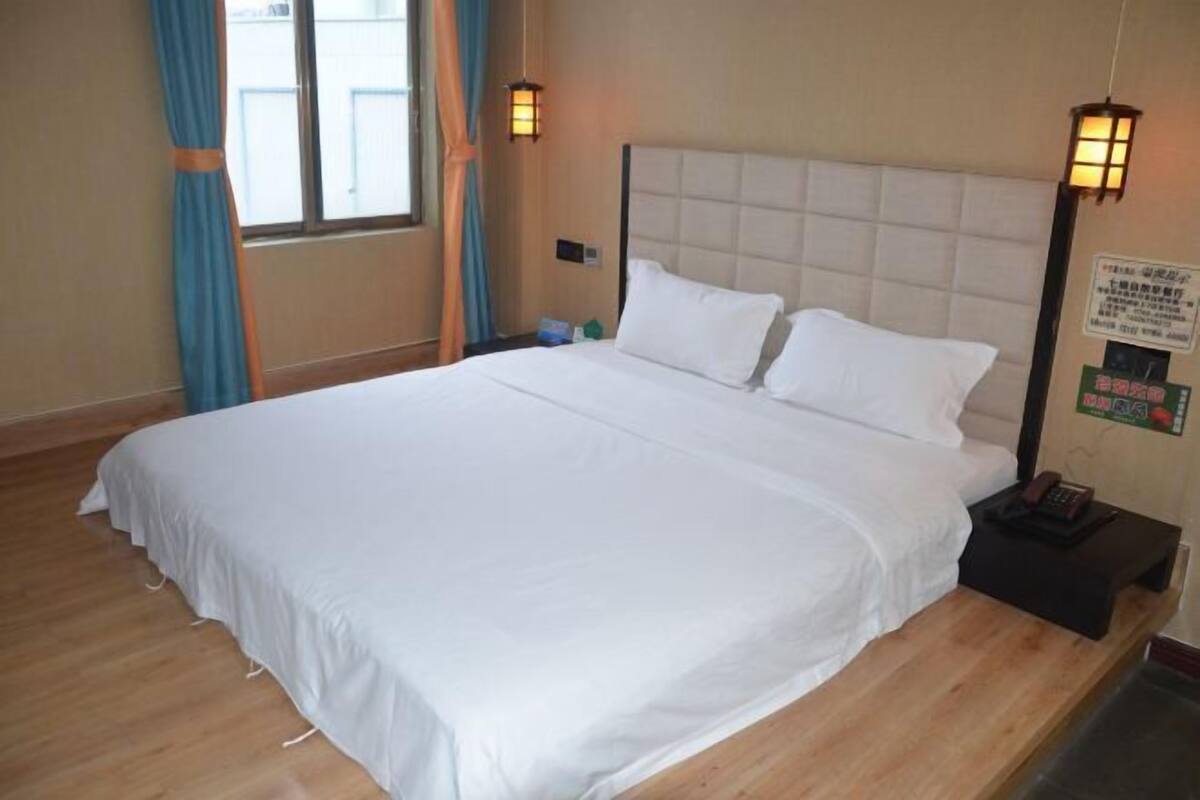A neatly made bed with white linens in a room with wooden flooring, a padded headboard, and two wall-mounted lamps.