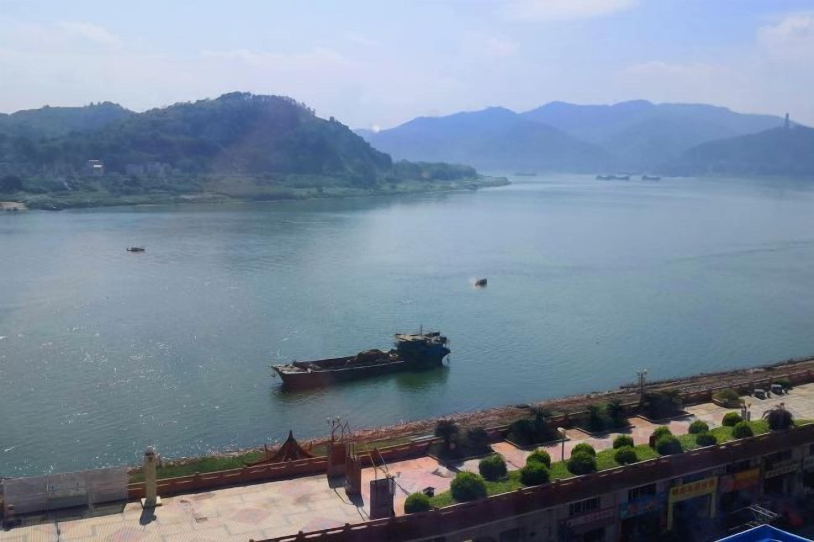 A river with boats, a bridge, and a hilly landscape in the background.