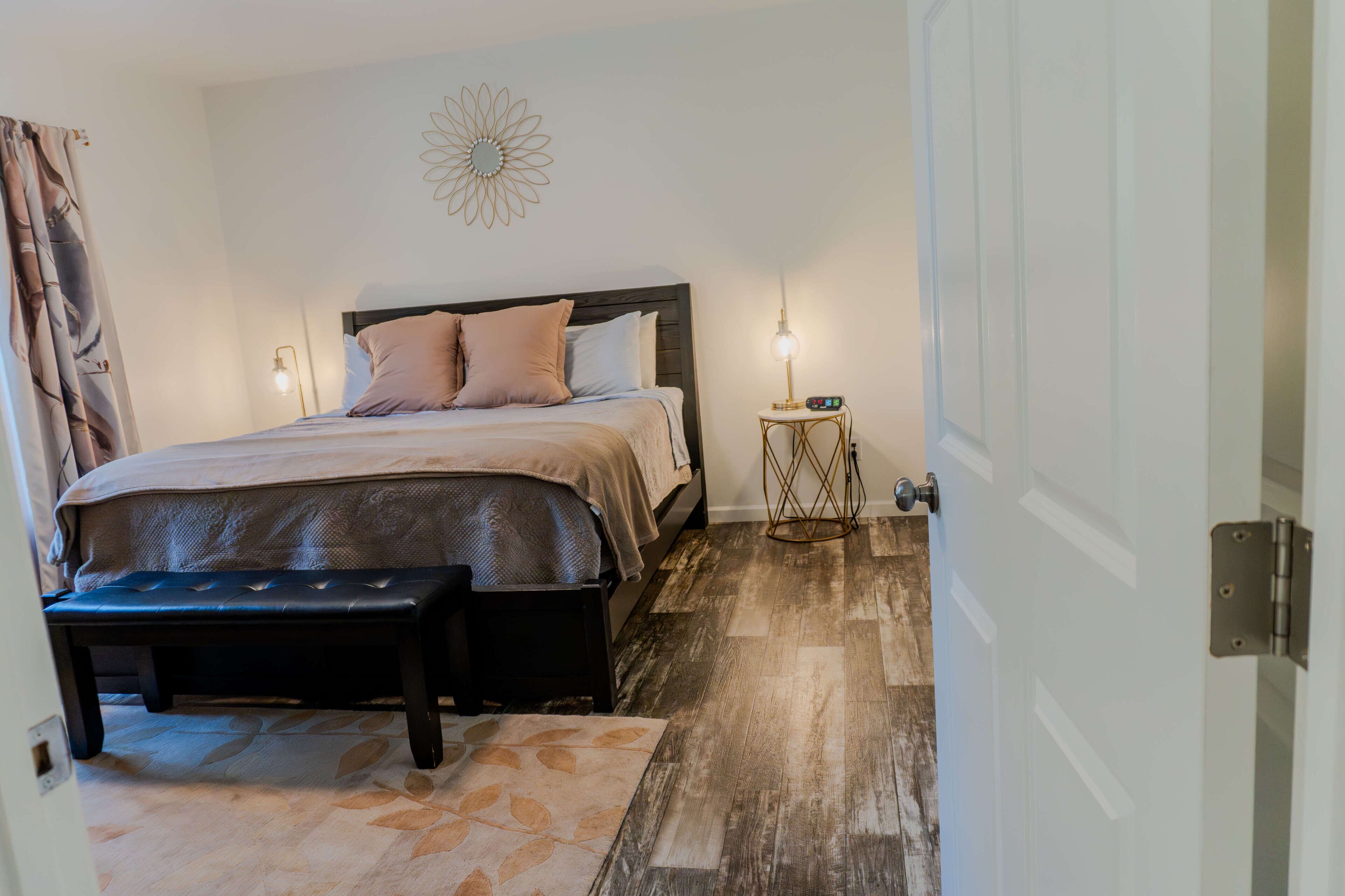 Une chambre à coucher comprenant un lit, un banc, une table de chevet, des éléments de décoration murale et une porte.