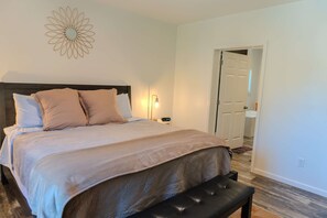 Una cama bien hecha con cabecera, una lámpara de noche y un banco al pie de la cama.