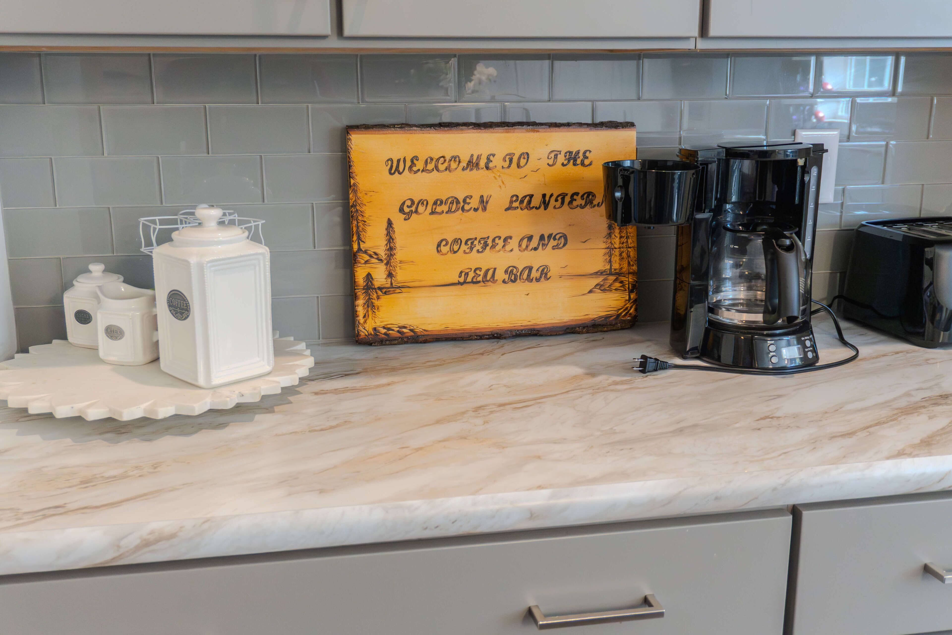 A kitchen with a coffee maker, a coffee grinder, and a sign that reads "Welcome to the Golden Ranger Coffee and Tea Bar."
