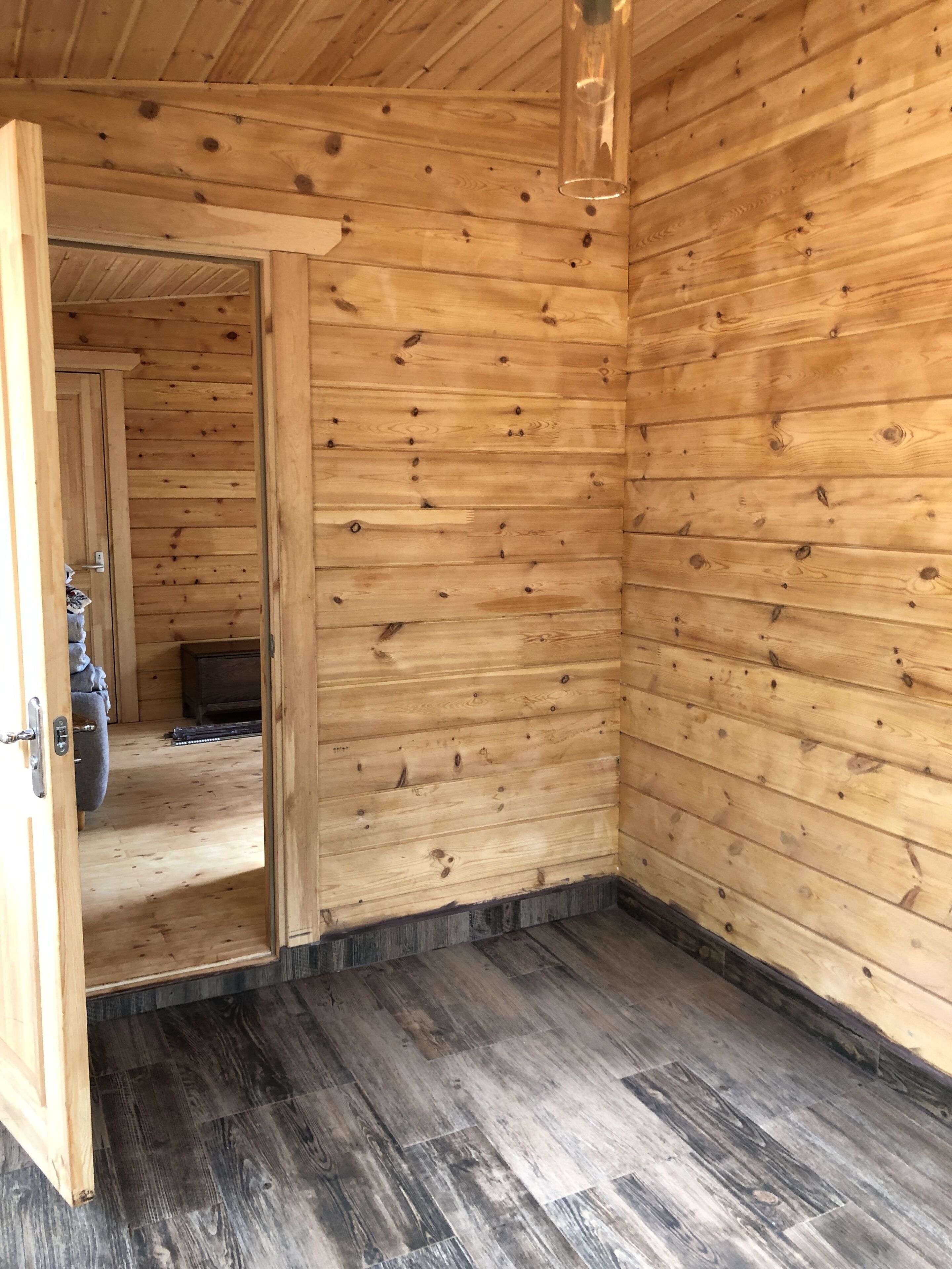 L’intérieur d’une cabane en bois, avec une porte en bois donnant sur une autre pièce, un plancher en bois et un plafond apparent.