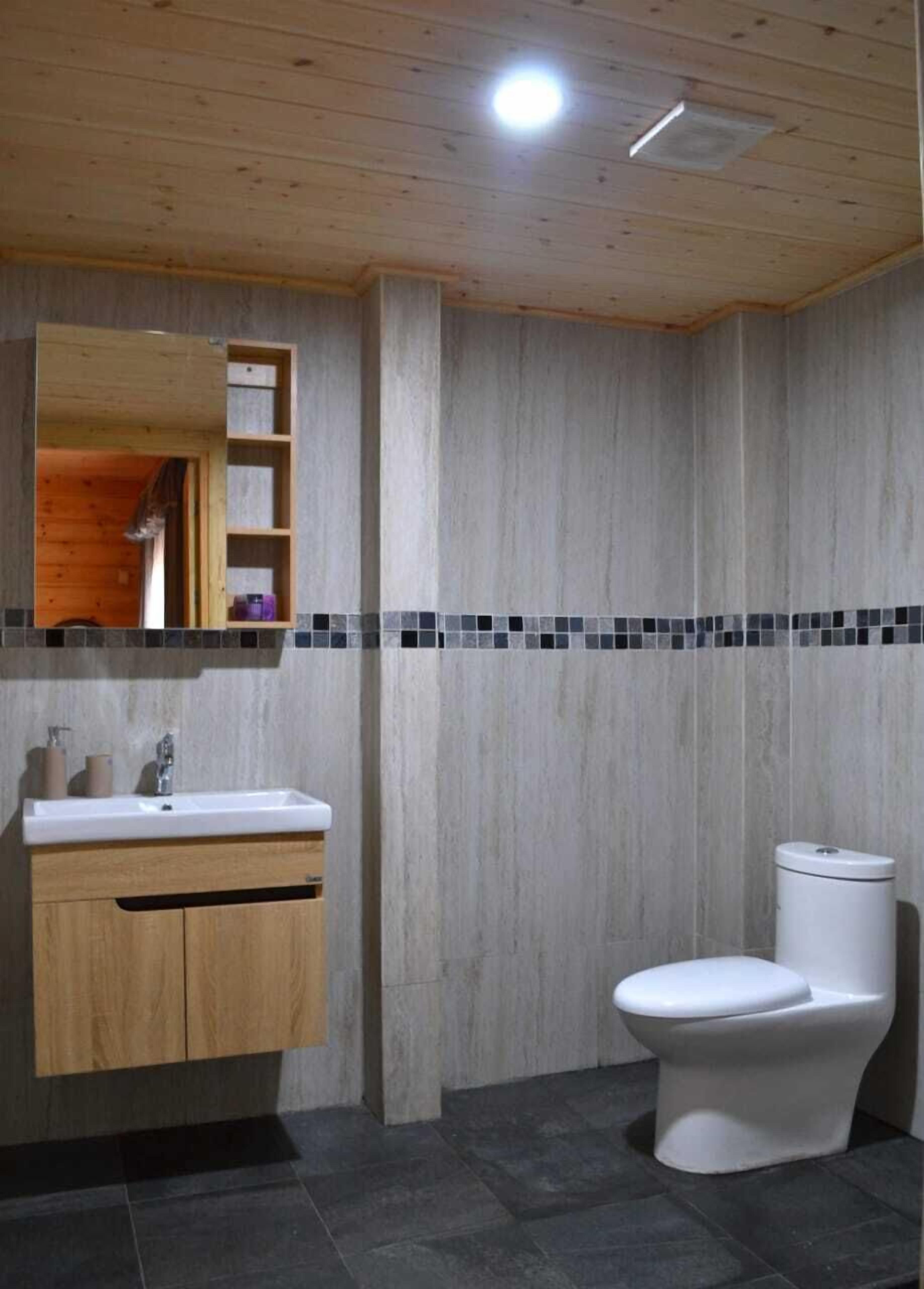 A bathroom with a wooden vanity, a white sink, a mirror, a toilet, and a tiled backsplash.