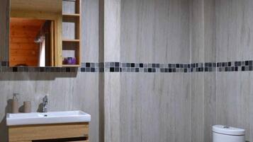 A bathroom with a wooden vanity, a white sink, a mirror, a toilet, and a tiled backsplash.