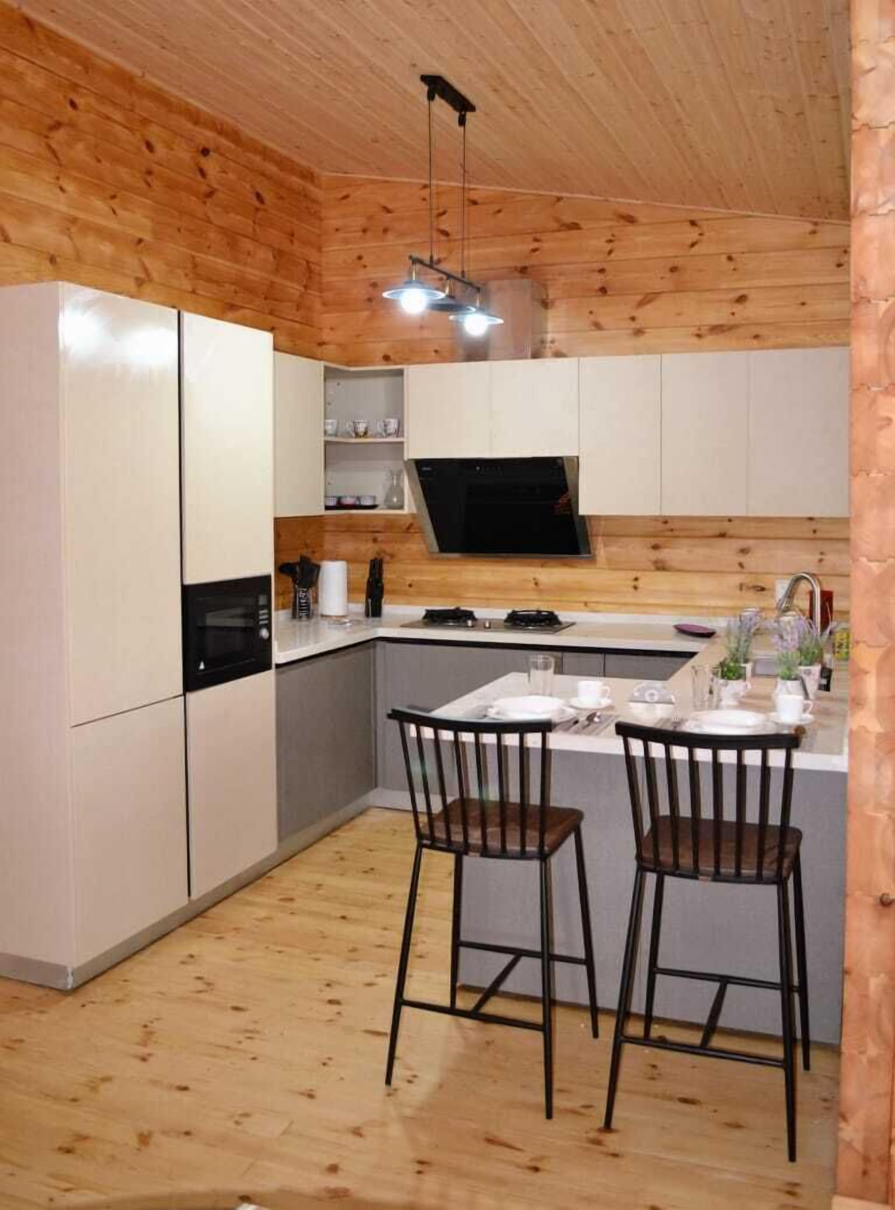 Een kleine keuken met witte kastjes, een magnetron en een fornuis. Twee houten stoelen staan bij een eettafel.