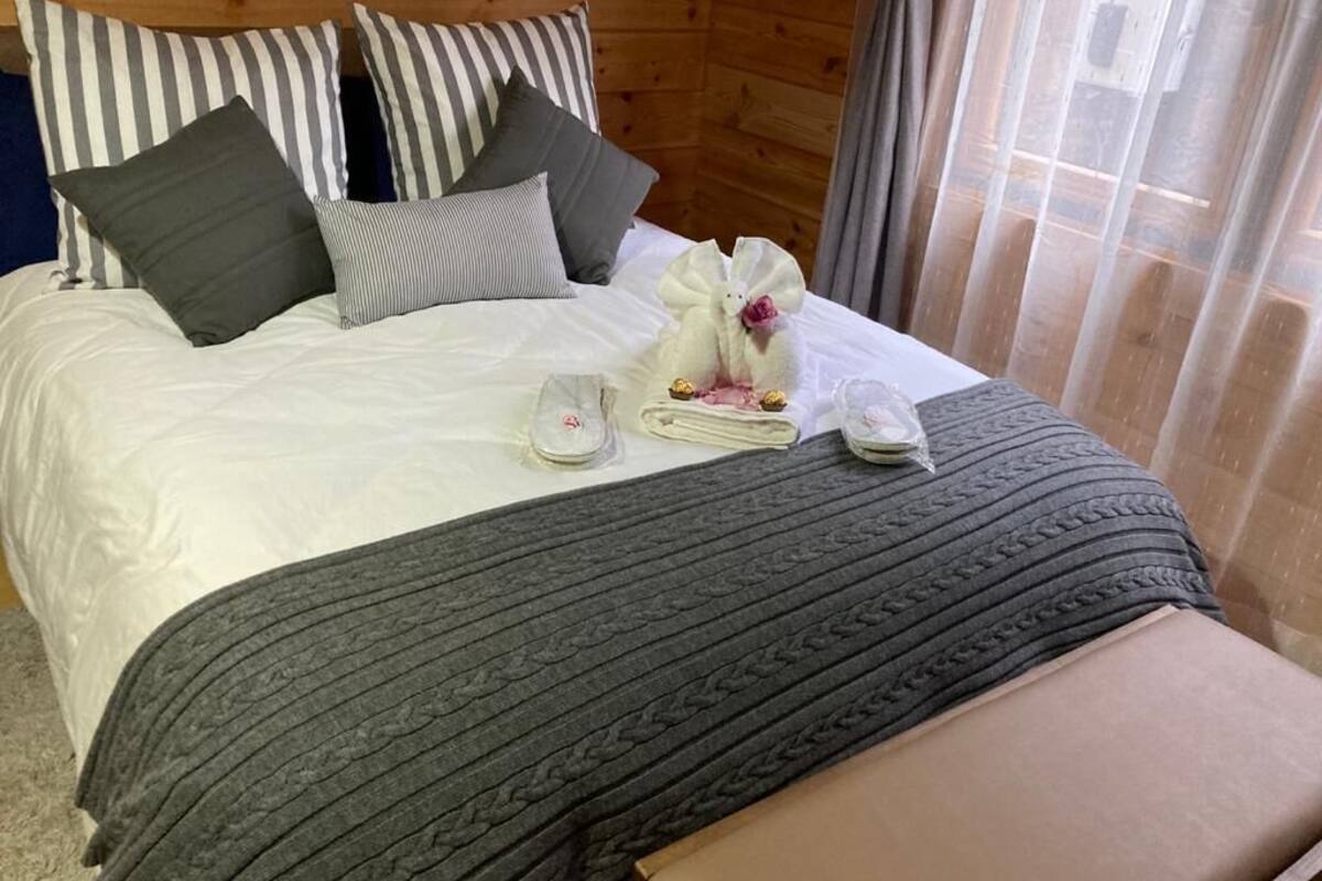 Cama bem arrumada com almofadas listradas, um cobertor cinza e um objeto decorativo branco sobre a cama.