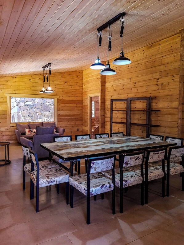 L'intérieur d'un chalet en bois, avec une grande table à manger, des chaises et des lampes suspendues.