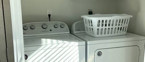 A laundry area with a front-loading washer and dryer, a white laundry basket, and a white cabinet above the dryer.