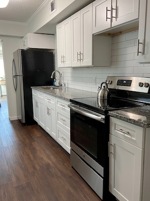A modern kitchen with white cabinets, stainless steel appliances, and a granite countertop.
