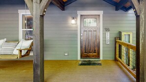 Une véranda en bois avec un paillasson, une porte dotée d’une fenêtre et un luminaire suspendu.