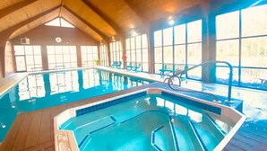 Une piscine intérieure à l’eau claire, dotée d’une terrasse en bois et de grandes fenêtres qui laissent entrer la lumière naturelle.