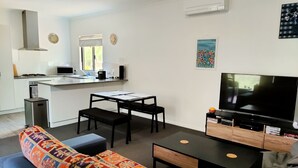 Un apartamento moderno con cocina, comedor y sala de estar. Cuenta con un sofá, una mesa de centro, un televisor y una pequeña mesita auxiliar.