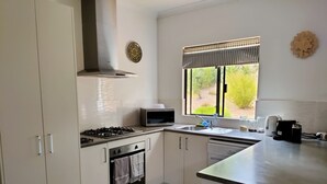 Una cocina moderna con armarios blancos, estufa a gas, microondas, pileta y ventana con vista a la vegetación.