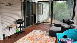 Un espacio al aire libre cubierto con una terraza de madera, un tapete colorido, una silla azul y una parrilla.