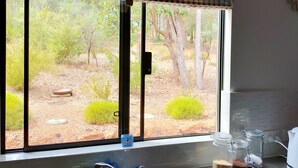 Una cocina con ventana que da a un jardín, un fregadero y una encimera con frascos y un hervidor.