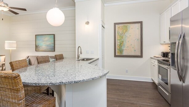 A kitchen with a central island, stainless steel appliances, and a dining area with wicker chairs. - King one-bedroom condo w/ pool in the SSI Village area Unit 2205 (Saint Simons Island)