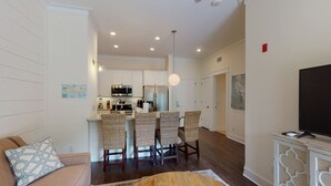 A modern living room with a sofa, a round coffee table, and a TV on a cabinet. There is a kitchen area with a dining table and chairs. - King one-bedroom condo w/ pool in the SSI Village area Unit 2205 (Saint Simons Island)